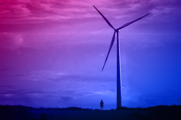 A wind turbine against a dark sky, a small silhouette of a man n